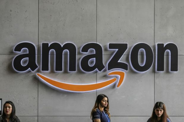 Employees stand near a company logo. - Dhiraj Singh/Bloomberg